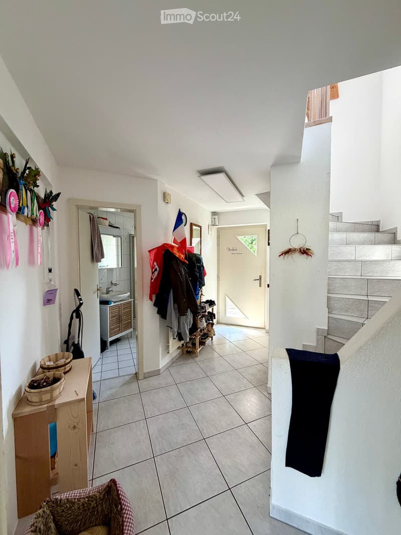 Hallway with tiled floor, coat rack, small wooden shelf, staircase leading upwards, and a small pet bed in the foreground.