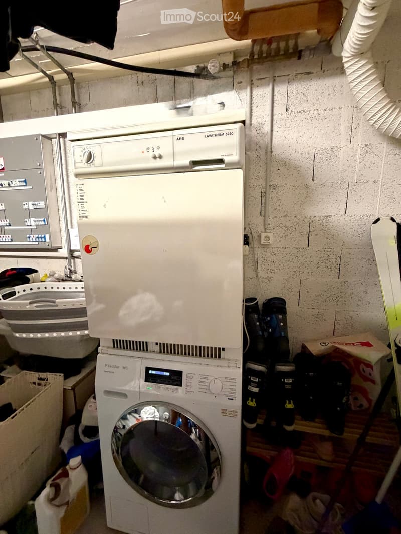 A small bathroom with a washing machine and a dishwasher stacked together, a sink with a faucet, and various items stored around the room.