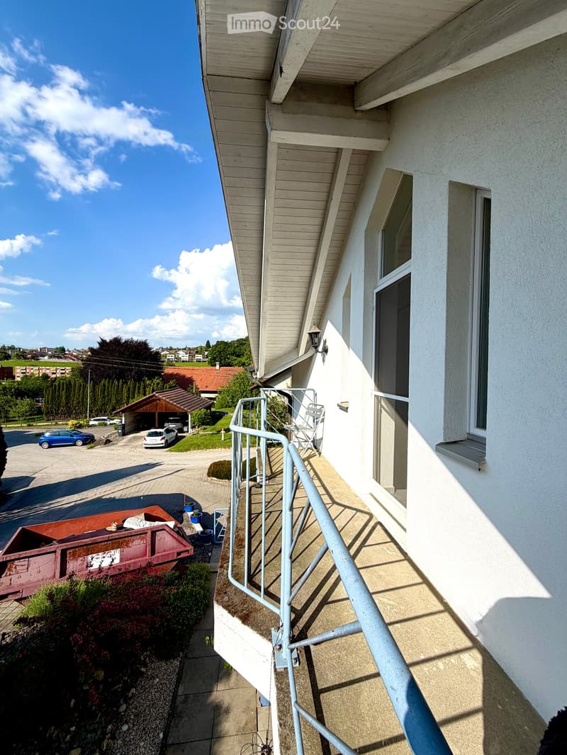 Balcony with metal railing, white folding chair, and a view of the street and surrounding buildings.