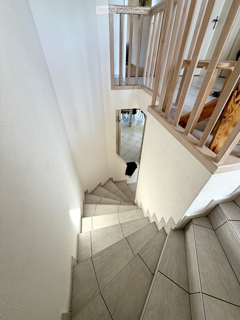 Spiral staircase with wooden handrails and tiled steps, leading to an upper level with visible room and furniture.