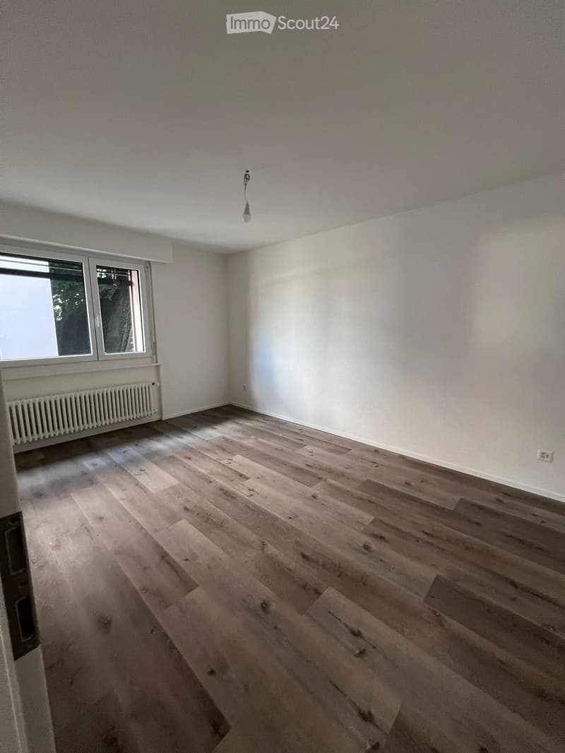 Empty room with wooden flooring, white walls, and a window with a radiator below it.