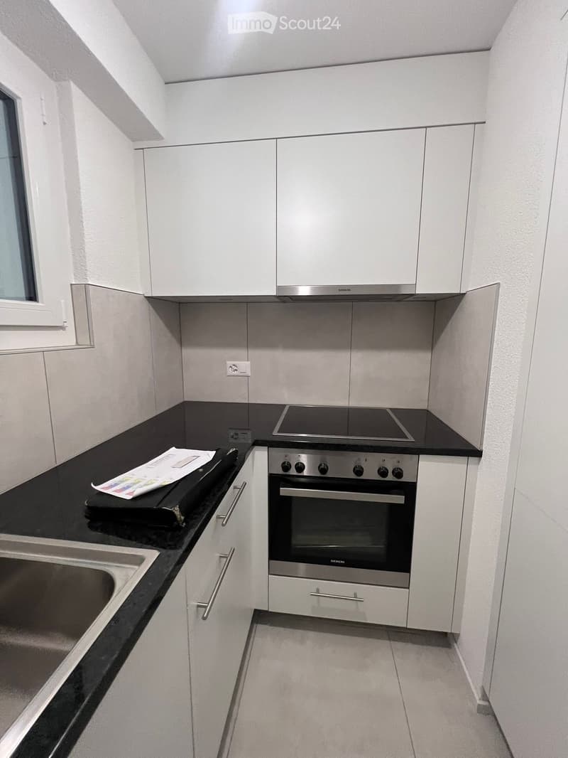 Modern kitchen with white cabinets, black countertop, stainless steel oven, and sink.