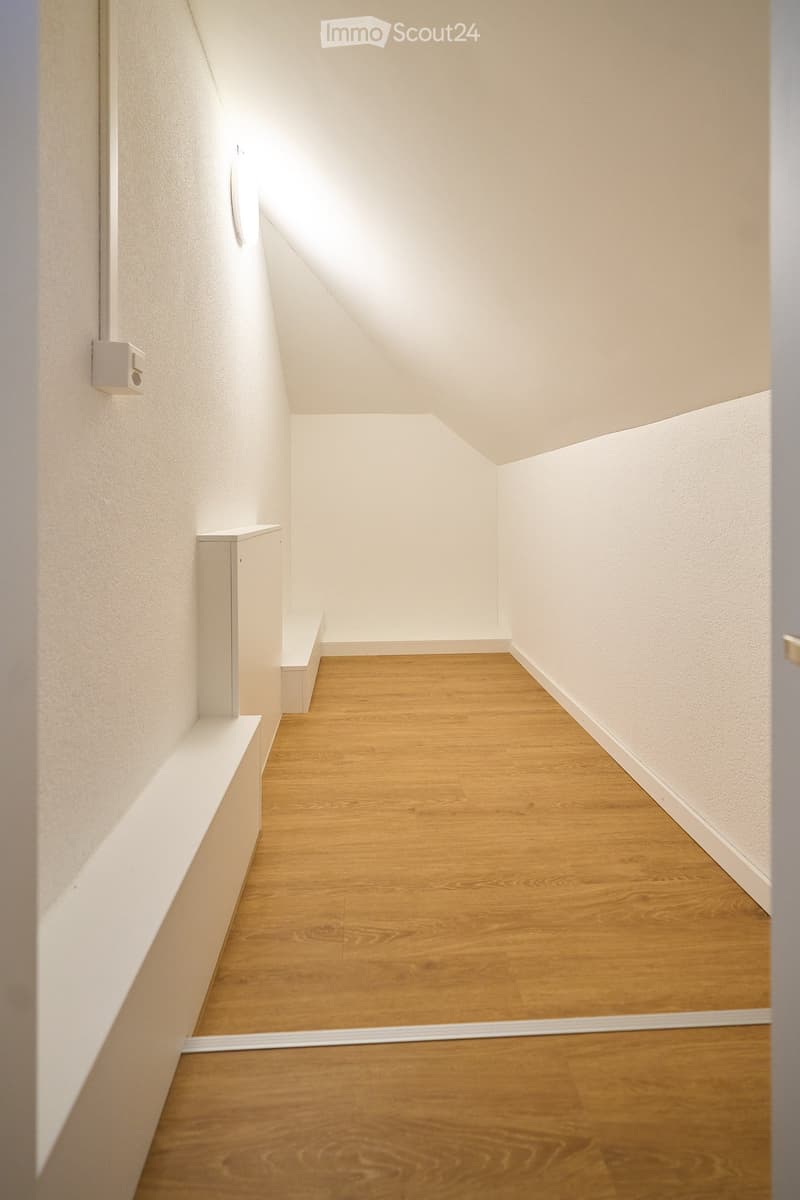 Empty hallway with wooden flooring and white walls, featuring built-in storage shelves on one side.