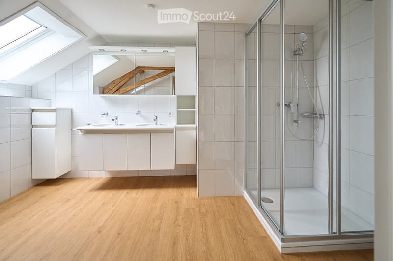 Modern bathroom with wooden flooring, white tiled walls, a double sink vanity with mirrored cabinet, and a glass-enclosed shower stall.
