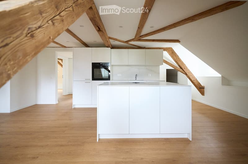 Modern kitchen with white cabinets, a central island, and a built-in oven. The space features exposed wooden beams and a wooden floor.