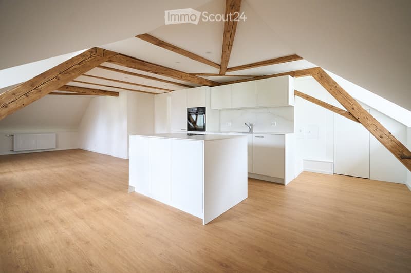 Modern kitchen with white cabinets, a central island, and exposed wooden beams on the ceiling. The floor is made of light wood, and the backsplash features a marble design.
