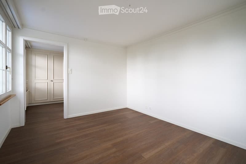Empty room with white walls, wooden flooring, and a doorway leading to another room. No furniture or equipment is present.