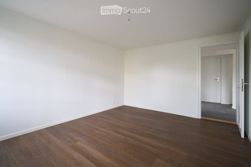 Empty room with wooden flooring and white walls, featuring an open doorway leading to another room.