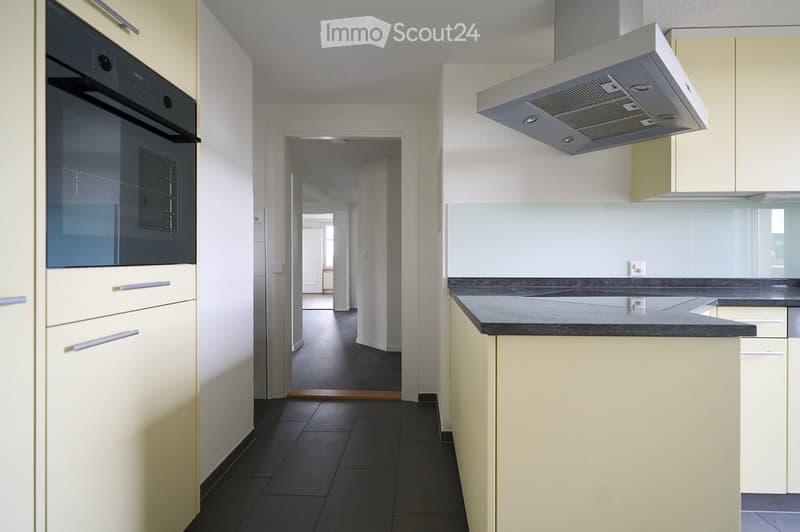 Modern kitchen with light-colored cabinets, dark countertops, built-in oven, and range hood. The space is clean and organized with a visible doorway leading to another room.