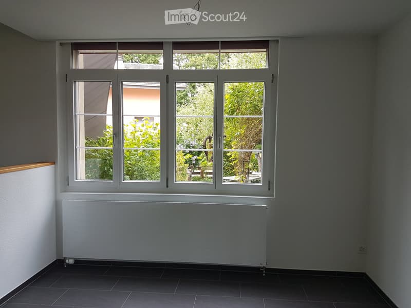 Empty room with large windows, radiator, and dark tiled floor.
