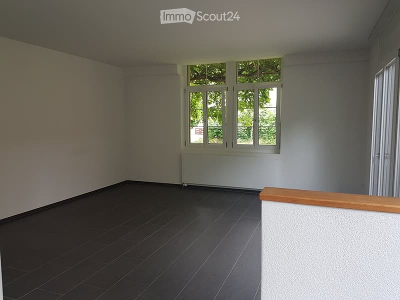Empty room with dark tiled floor, light-colored walls, large windows, and a radiator below the windows.