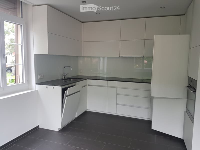 Modern kitchen with white cabinets, black countertops, and a stainless steel sink.