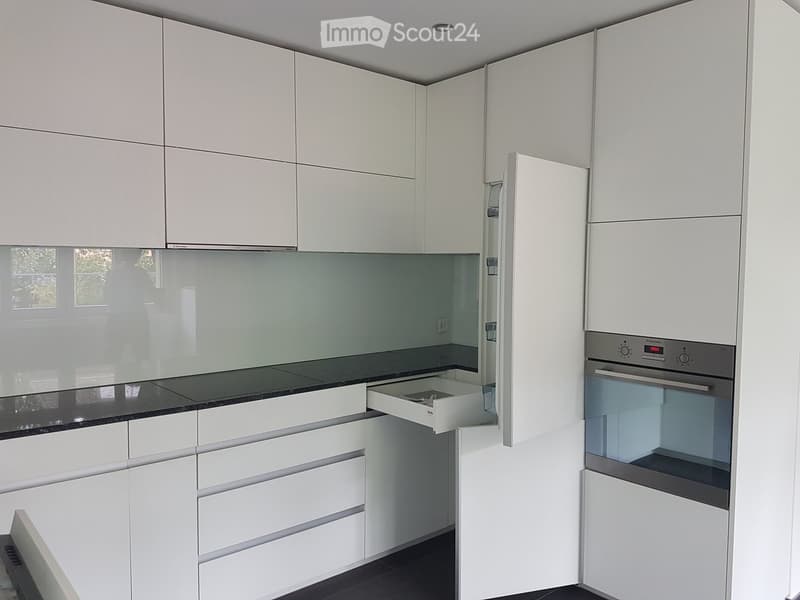 Modern kitchen with white cabinets, black countertop, and built-in oven.