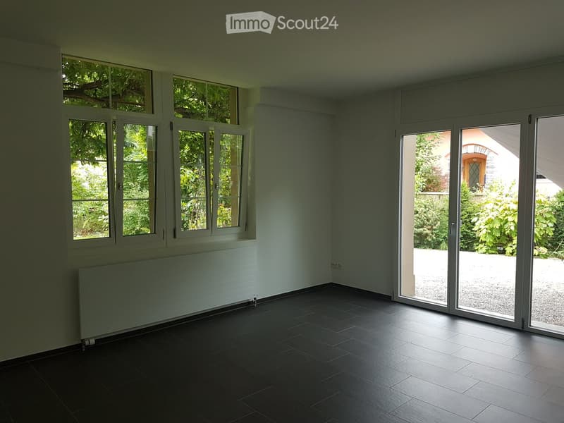 Empty room with dark tiled floor, white walls, large windows, and sliding glass doors leading to an outdoor area.