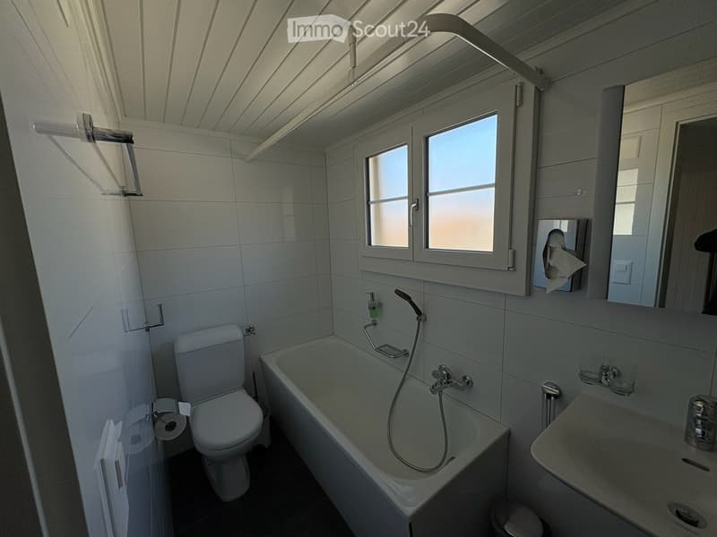 Bathroom with white tiles, toilet, bathtub, sink, mirror, and various fixtures.
