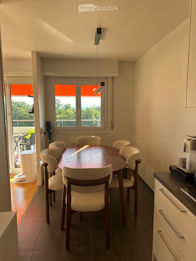 Dining area with a round wooden table, six chairs, and a coffee machine on the counter.