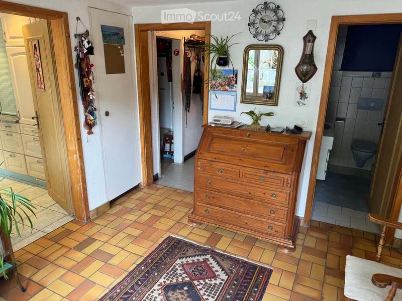 Hallway with tiled floor, wooden dresser, mirror, clock, and open doors leading to other rooms.