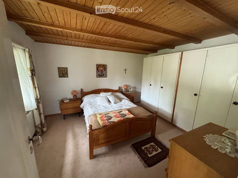 Cozy bedroom with wooden bed, nightstands, and a small table. Features a wooden ceiling and white walls.