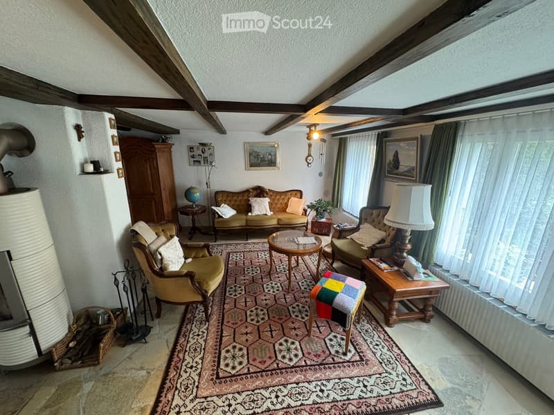 Cozy living room with exposed wooden beams, a patterned rug, a sofa, armchairs, coffee table, table lamp, globe, and a fireplace.