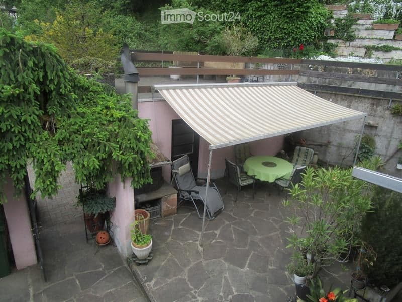 Private outdoor patio with stone flooring, covered seating area with a table and chairs, surrounded by potted plants and greenery.