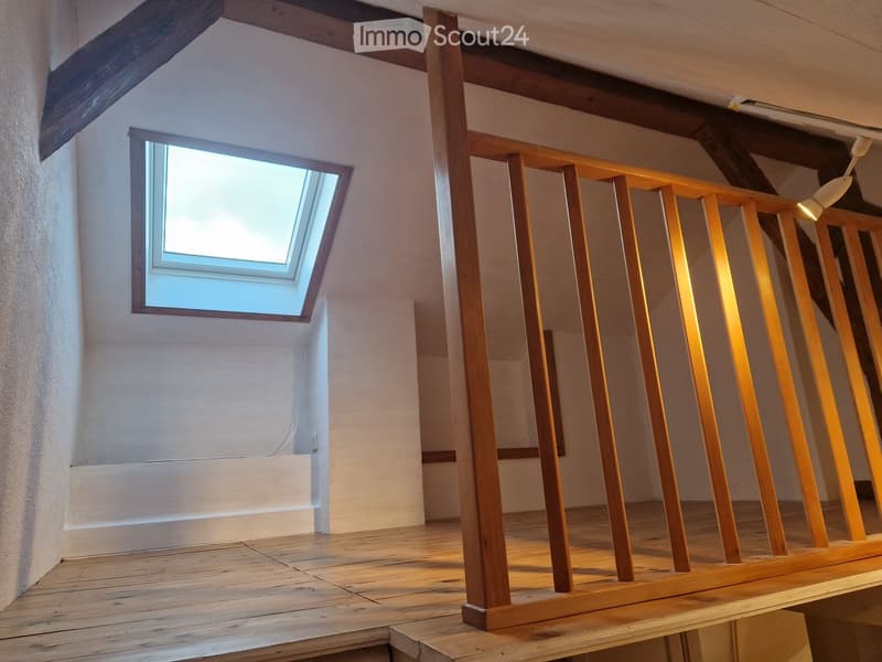Empty room with wooden floor, exposed wooden beams on the ceiling, and a skylight window allowing natural light to enter.