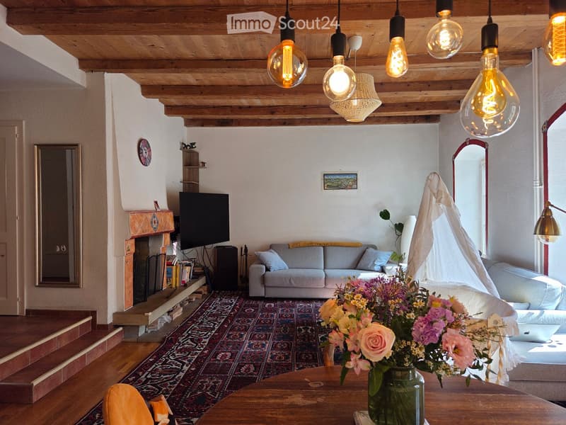 Living room with exposed wooden ceiling, fireplace, sofa, coffee table, and decorative vase with flowers.