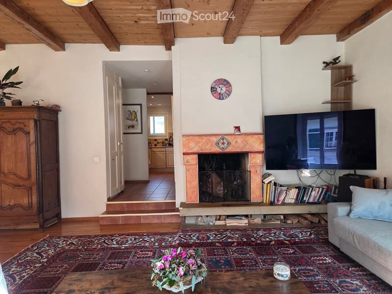 Living room with exposed wooden beams, fireplace, large television, sofa, coffee table, bookshelf, and decorative items.
