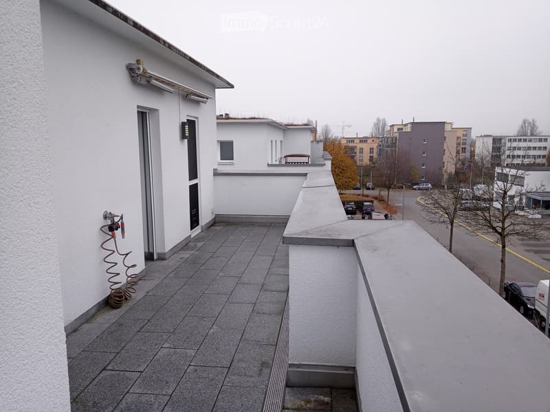 Balcony with tiled floor, white walls, and a view of surrounding buildings and parking area.