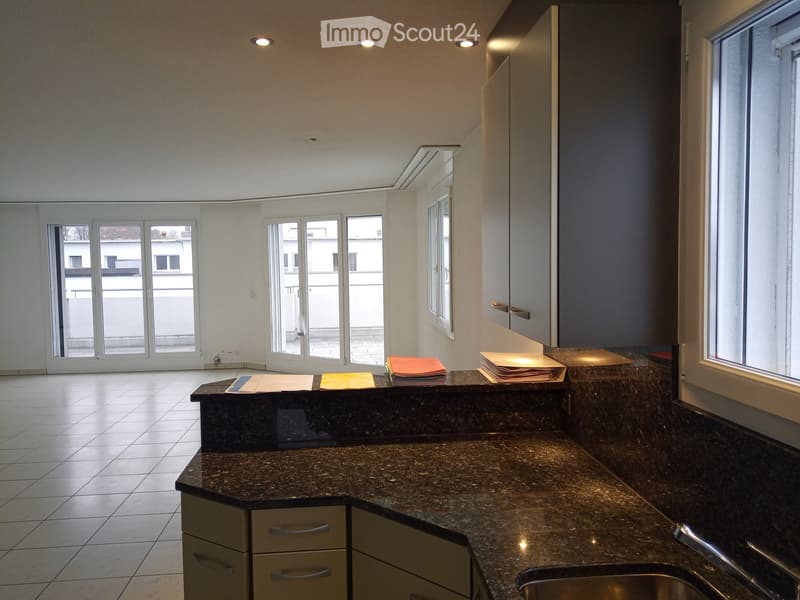 Modern kitchen with granite countertops, stainless steel sink, and built-in cabinets. Large windows and sliding glass doors provide natural light and access to a balcony.