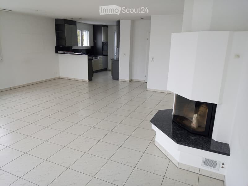 Open-plan living and dining area with a fireplace, white tiled floor, and a modern kitchen area with cabinets and appliances.