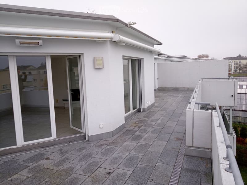 Roof terrace with tiled flooring, white walls, sliding glass doors, metal railing, and a view of the surrounding area.