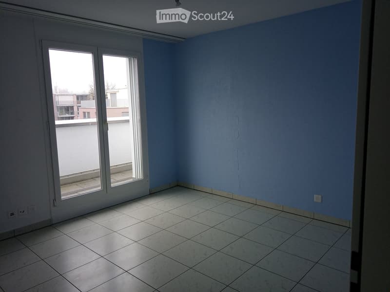 Empty room with light blue walls, tiled floor, and large sliding glass doors leading to a balcony.
