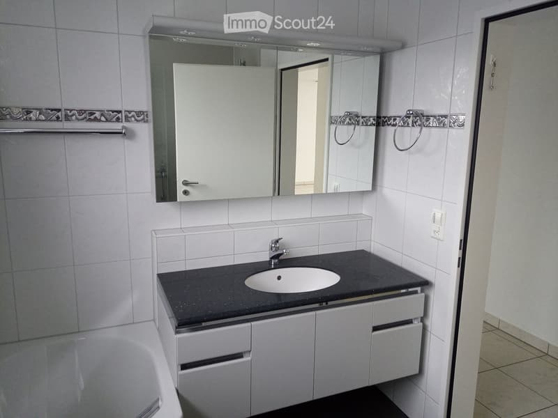 Modern bathroom with white tiles, a black countertop sink, a large mirror with built-in cabinets, and a bathtub.