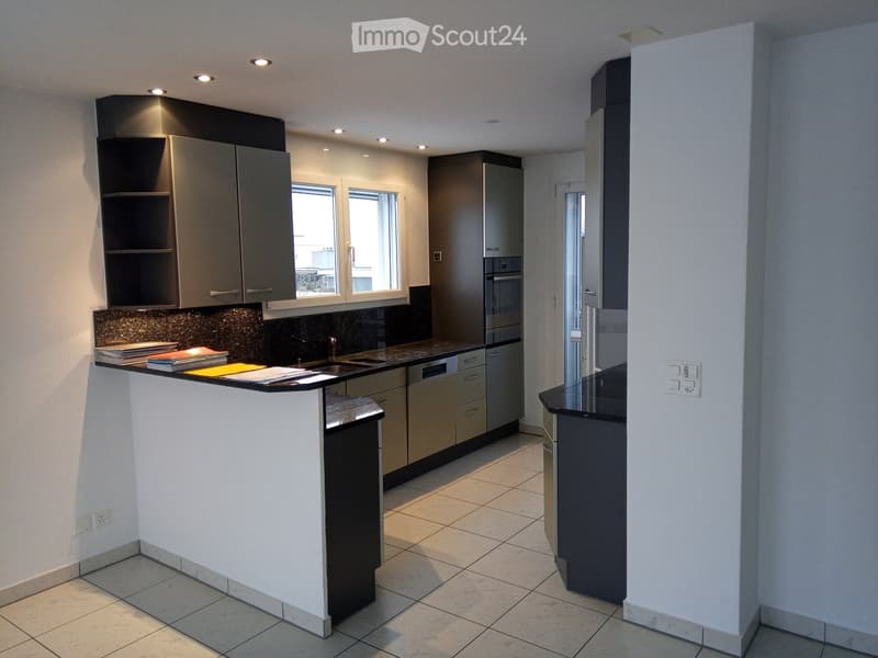 Modern kitchen with grey cabinets, a white island, and a dark countertop. Features include a sink, refrigerator, and oven, with a window providing natural light.