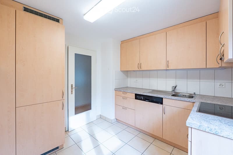 Modern kitchen with light wooden cabinets, tiled floor, and granite countertops. Features a sink, faucet, and dishwasher.
