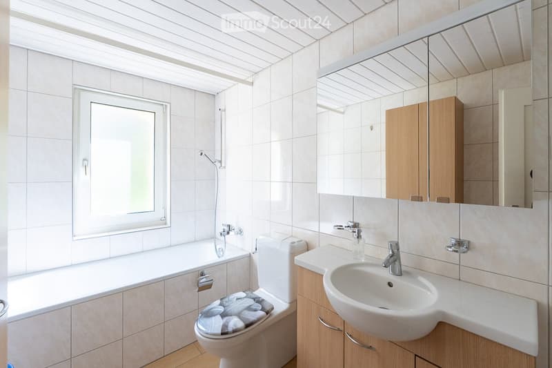 Modern bathroom with white tiles, a bathtub, toilet, sink, and a large mirror with wooden cabinets.