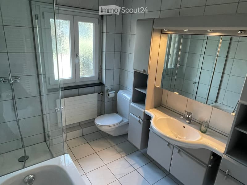 Modern bathroom with tiled walls and floor, featuring a bathtub, shower, toilet, sink, and mirrored cabinet.