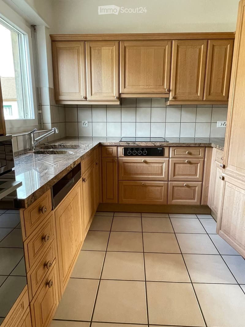 Modern kitchen with light wooden cabinets, granite countertops, and tiled flooring. Features a sink with a modern faucet, an oven, and ample cabinet storage.