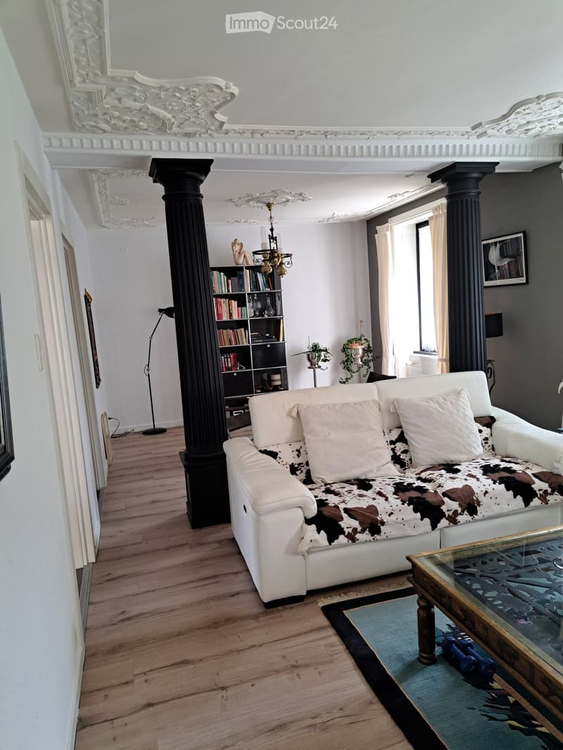 Elegant living room with white leather sofa, cowhide throw, glass coffee table, bookshelf, floor lamp, and chandelier.