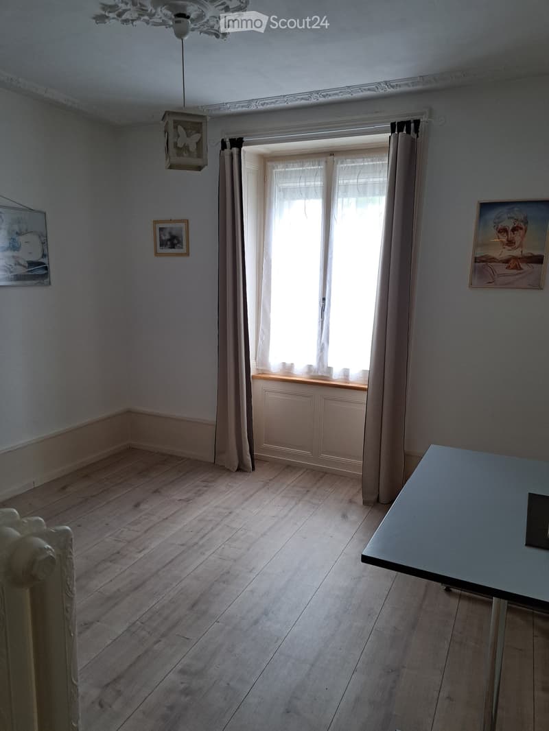Empty room with wooden flooring, large window with curtains, built-in cabinet, and decorative wall art.