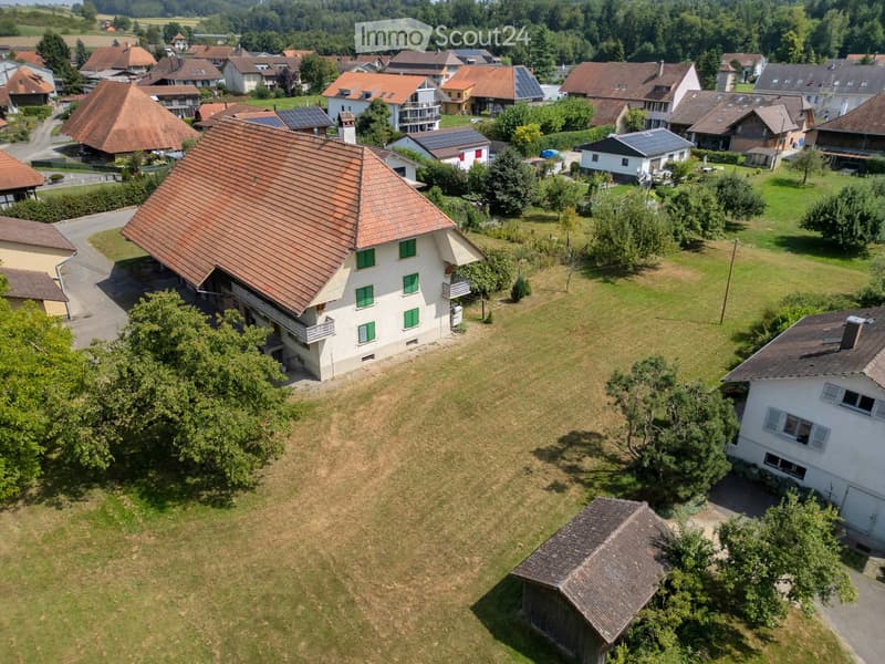 Aerial view of a residential area with multiple houses, green lawns, trees, and solar panels on some roofs.