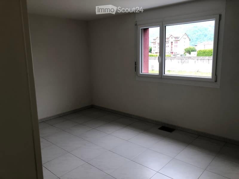 Empty room with tiled floor and large window showing a view of buildings and greenery outside.