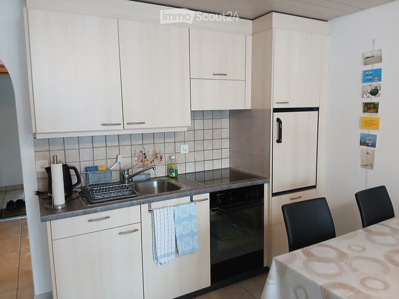 Modern kitchen with white cabinets, stainless steel sink, oven, and a small dining area with a table and chairs.