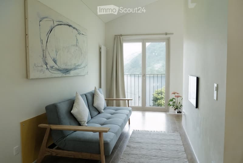 Modern living room with a grey sofa, wooden coffee table, side table, and a view of a mountain through large windows.