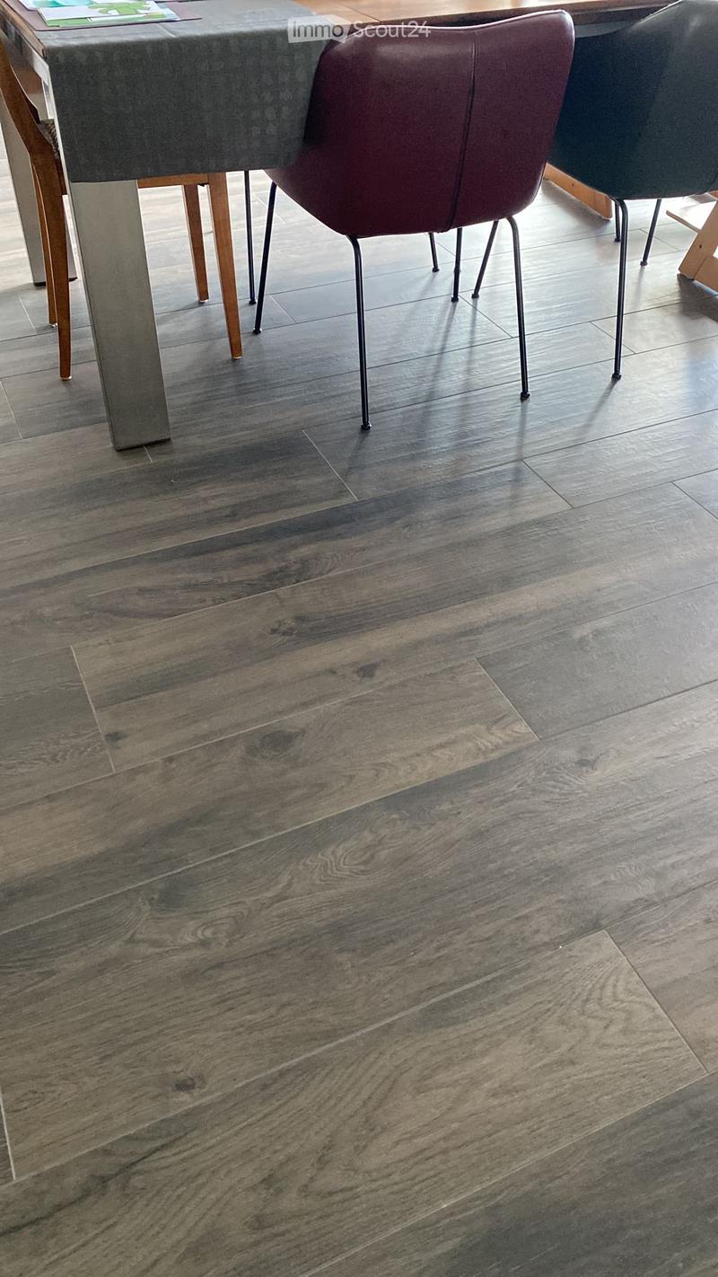 Empty room with dark wood flooring and a grey table with a maroon leather chair in the background.