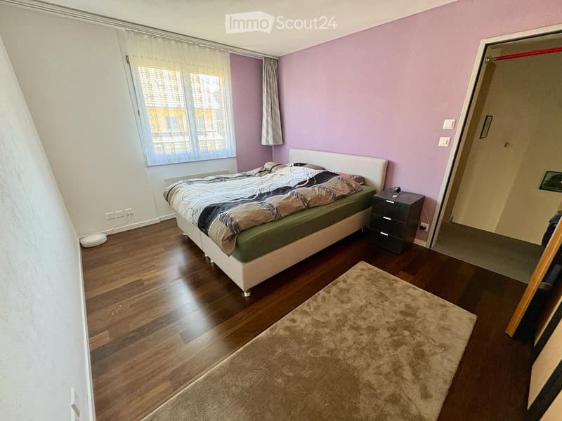 Bedroom with wooden flooring, a bed with a white headboard, a nightstand, a rug, and a mirror on the wall.