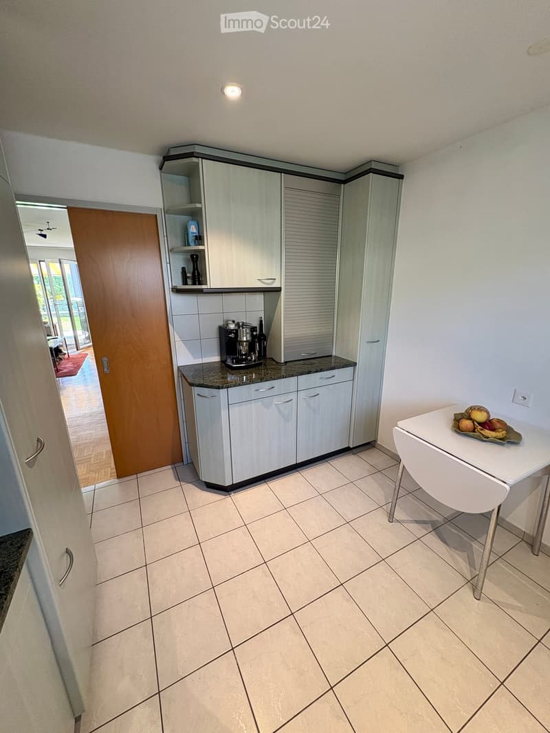 Modern kitchen with white cabinets, granite countertop, coffee maker, and a small table with a bowl of fruit.