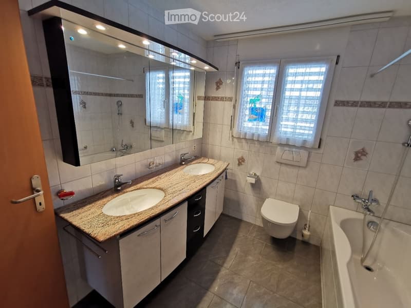 Modern bathroom with double sink, toilet, bathtub, large mirror, and tiled walls.