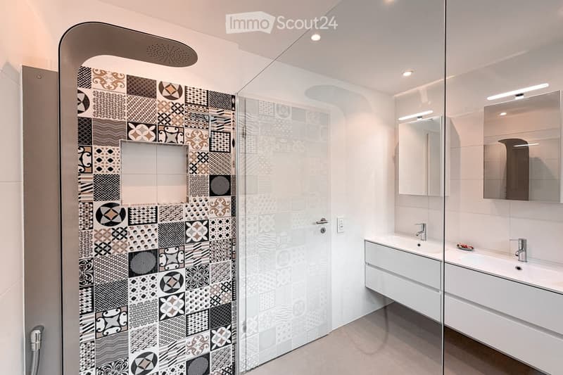 Bathroom. Modern bathroom with a glass-enclosed shower featuring patterned tiles, a white sink with a modern faucet, and a large mirror with built-in lighting.