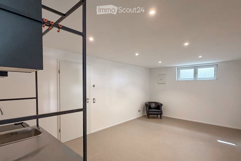Furnished Room. Modern, minimalist room with white walls, a single black leather chair, a sink, and a door leading to another space.